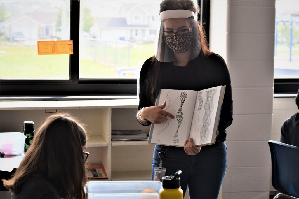Elementary art teacher standing infront of a student holding a book with an art example.
