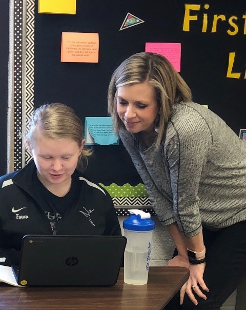 Seated student working with her teacher looking over her shoulder.